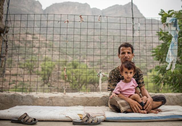 A man sits outside holding his child in his lap in a mountain village in Yemen where an IRC mobile health team provides care to families affected by conflict.
