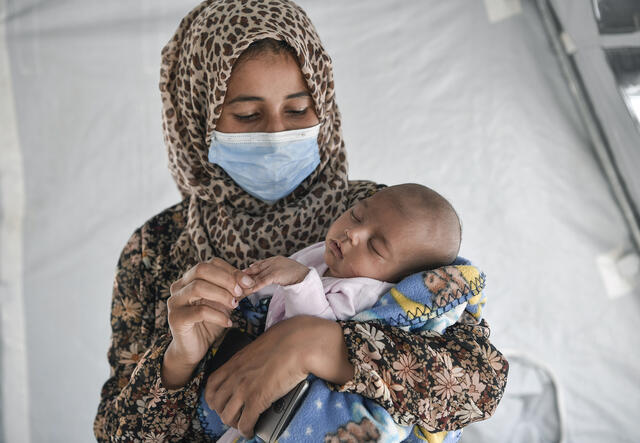 Ikram Ismail holds her infant daughter, touching her tiny fingertips