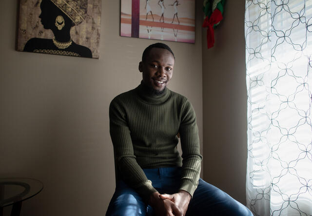 Fredrick Shema sitting on a stool in his home next to a window. 