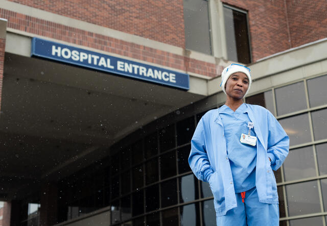 Nabila in front of the hospital where she works. She is wearing blue scrubs. 