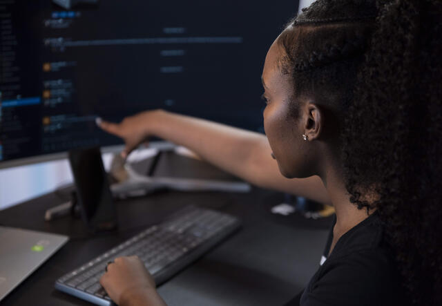 Diana sits at a computer and points to the screen