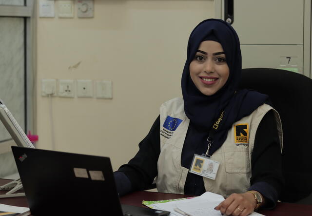 Dr. Bushra sits smiling at a desk at an IRC office in Yemen, her laptop computer in front of her.