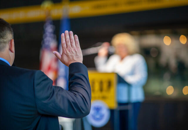 A view of man from the back raising his hand, taking an oath during a naturalization ceremony.