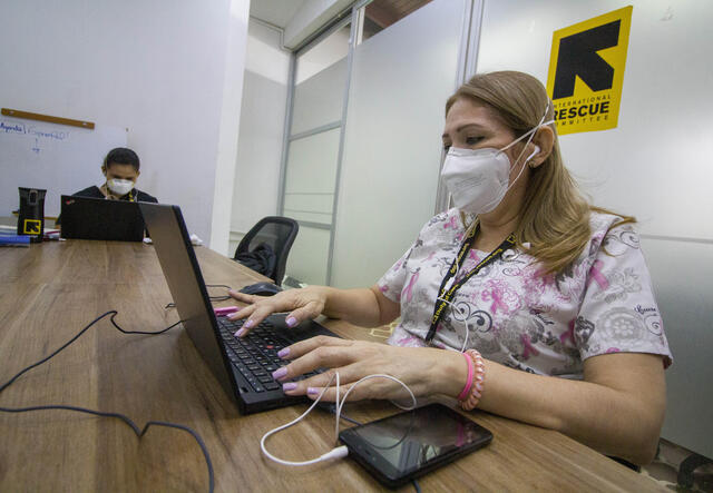 An IRC health worker in Colombia, wearing a mask to prevent the spread of COVID 19, types at her laptop in an IRC office.