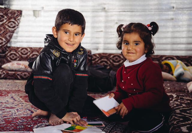 5-year-old Syrian boy Ayham and his 3-year-old sister Reham sit on a mat playing with a puzzle.