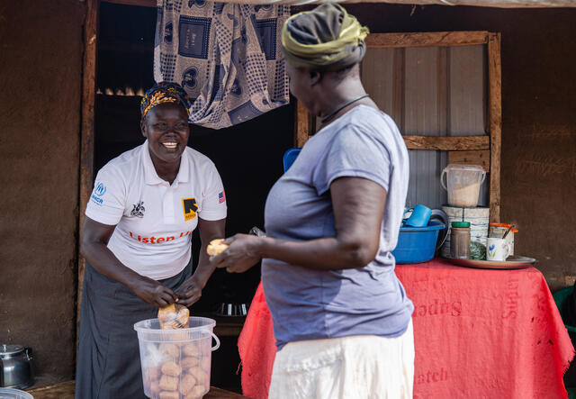 South Sudanese refugee Jemimah Sadia, holding a plastic bag of small cakes, speaks with a customer at her small tea shop in a Ugandan refugee camp.olding a 
