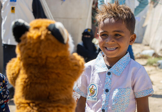 Outside in Al-Manshar camp, five-year-old Yasser laughs while looking at a fox puppet 