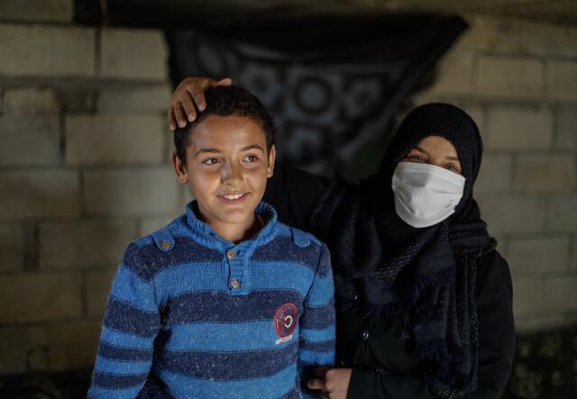 Muna stands next to her son Tareq with her hand on his head. 