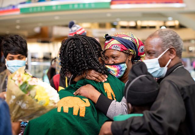 Mauwa hugs her mother while her father, son and other family members stand nearby in the airport. 