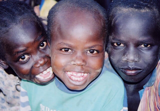Three refugee boys, known as the "Lost Boys," pose for a photo together--two smiling, one with a serious expression.
