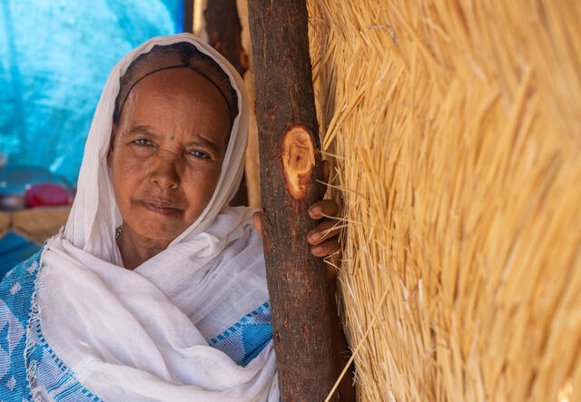 60-year old Berhan  leans on a post under a thatched roof