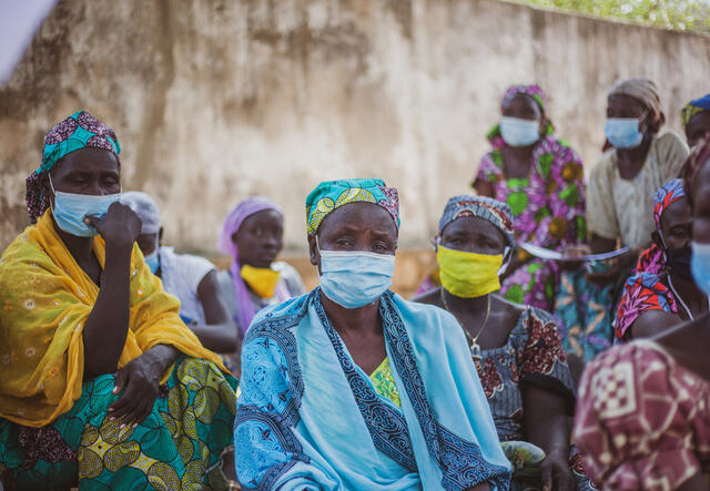 54-year-old Zara Tapita sits outdoors surrounded by other parents at an IRC Safe Space for children in Cameroon.