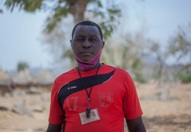 41-year old Komonda stands outside an IRC Safe Space in northern Cameroon, near a tree on a bright day.