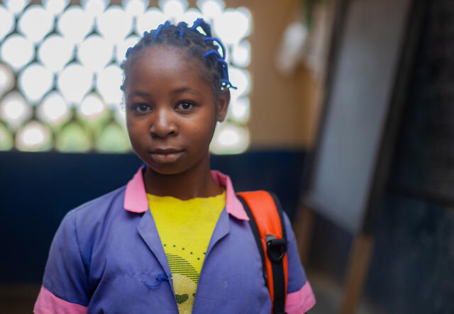 11-year old Kauvaumah stands in a classroom with her backpack slung over her shoulder.