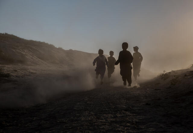 Children run through a desert and mountain landscape. The light is such that their faces are obscured. 