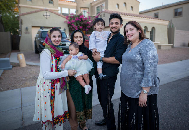 A family of six pose smiling outside of their home. 