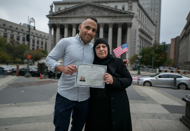 A refugee woman holds up her certificate outside of a building in Manhattan.