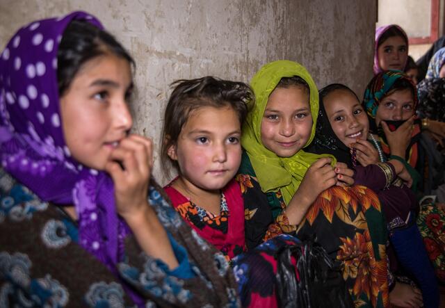 Several Afghan girls sit next to each other along a wall in a Safe Healing and Learning space run by the IRC.