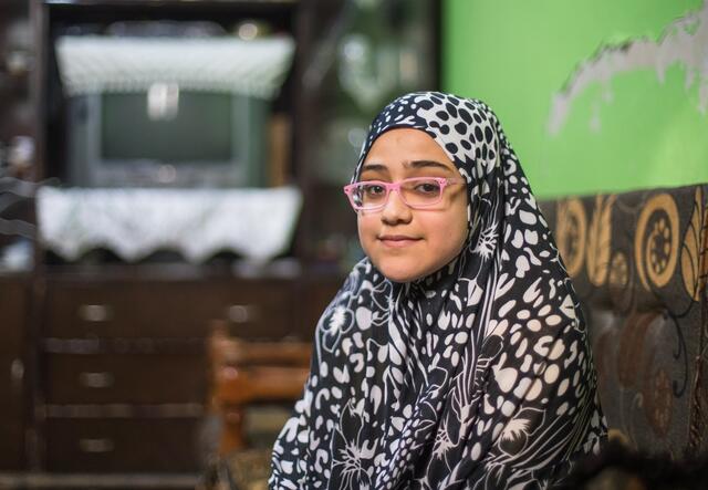 Salam, a 10-year-old Syrian girl wearing glasses, sits smiling for a photo.