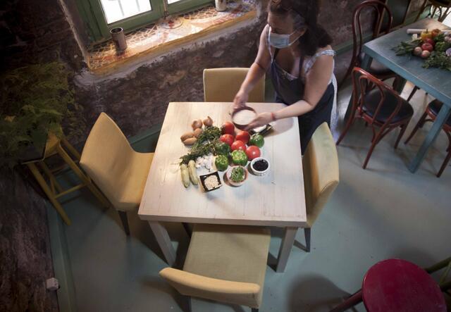 A woman holds a bowl of salt over a table of ingredients for stuffed tomatoes.