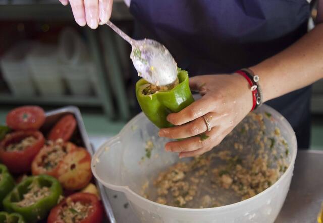 A woman adds filling to a green pepper.