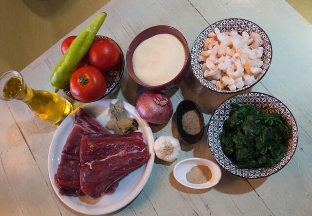 Raw tuna, tomatoes, spinach, garlic, onions, and other ingredients laid out on a table.