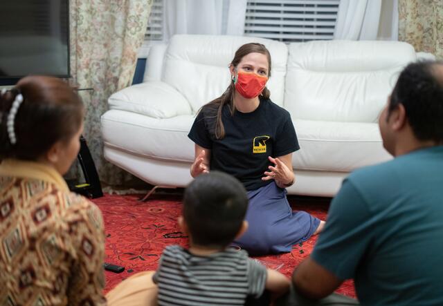 34-year-old Afghan translator Ali, is seen from behind seated on the floor with his wife and two young children as they speak with a female IRC staff member in Richmond, Virginia. 