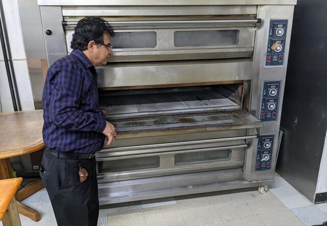 A storeowner standing next to a large oven.