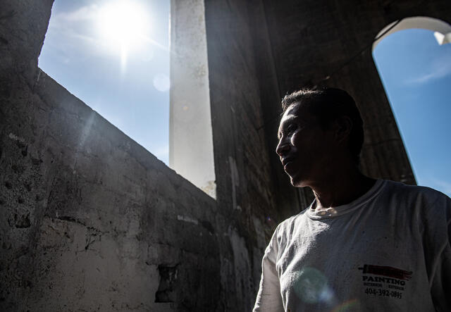 A Salvadaron man, Reynaldo, stands looking out at the sunshine through the window of a church he has been hired to paint.painting, 