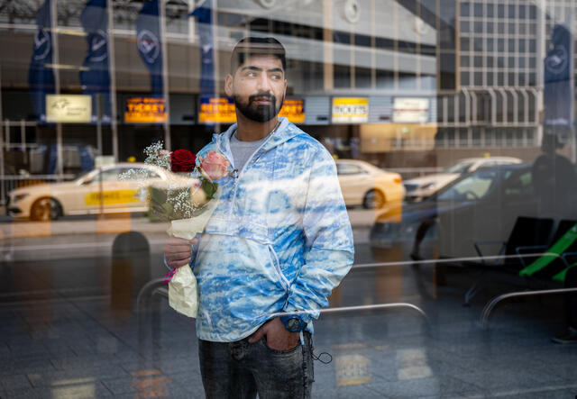 Afghan refugee Mehdi, 29, stands looking through a window at Frankfurt airport in Germany. He is holding flowers for his younger brother, whose flight is about to arrive.