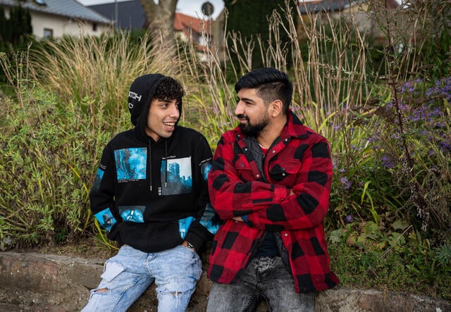 Afghan refugees Medhi and his teenage brother Ali, recently reunited in Germany, sit outside looking at each other and smiling as they talk.