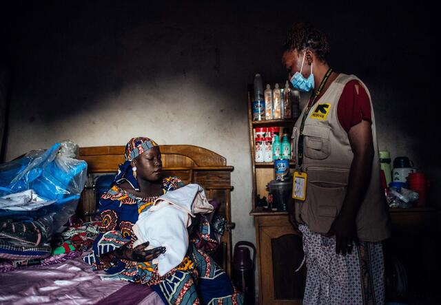 A Nigerian midwife watches over a woman and her baby, who is swaddled in a blanket