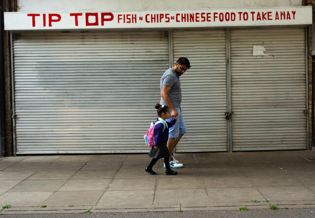 Maasom and his 4-year-old daughter walk hand in hand to school past a fish and chips shop in Andover, England.