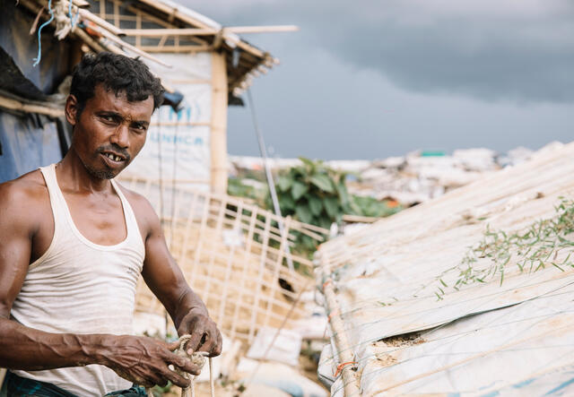 A man looks at the camera while standing in front of a caved in roof. 