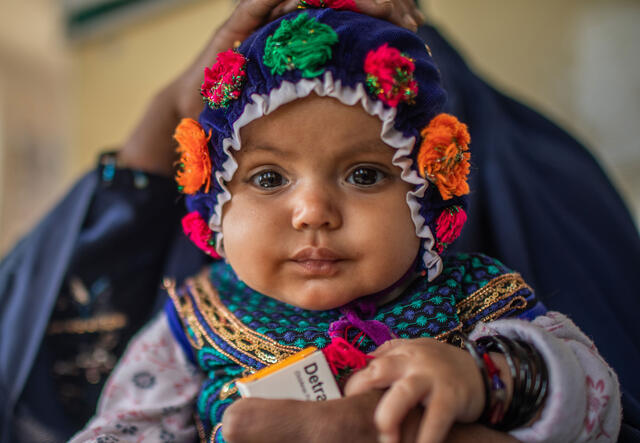 A close up of a baby wearing a bright colored hat sitting on their mothers lap.
