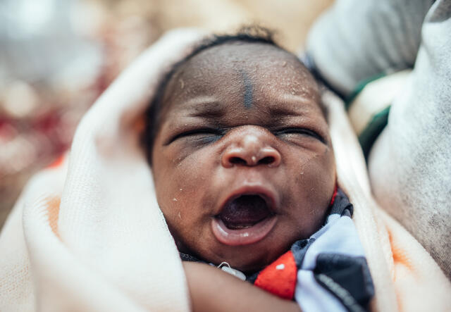 A close up of a seven day old baby wrapped in a blanket and yawning. 