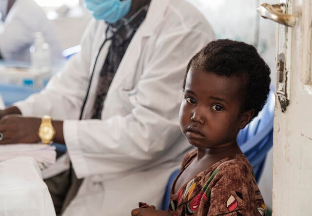 A young Somali child to be examined for malnutrition stands next to a health worker.