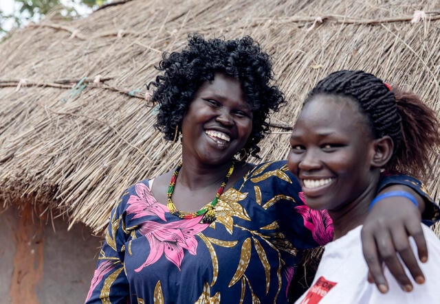 Smiling, two women look at the camera. One has her arm around the shoulders of the other. 
