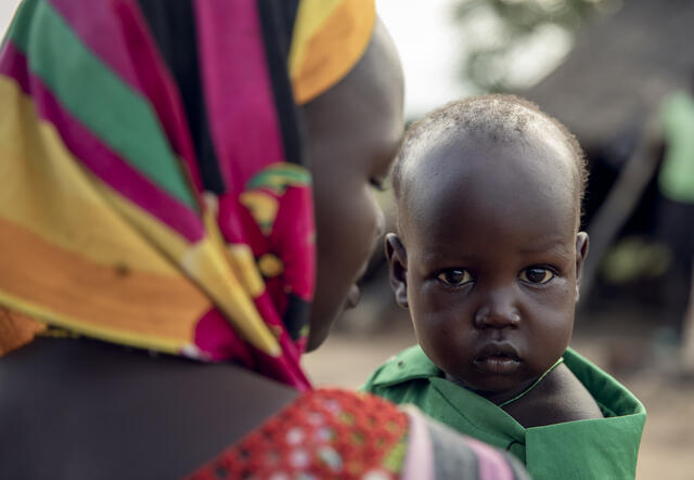 A close up of a mother holding her young son. He is looking at the camera and she is looking away.
