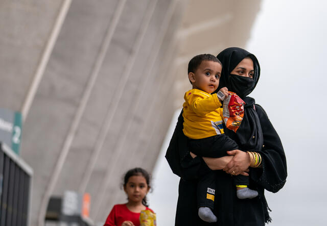 A woman holds a toddler outside Dulles International Airport while a young girl stands next to them. 