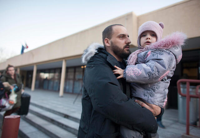 Dressed in winter jackets, a man holds his young daughter at a train station in Poland. 
