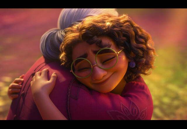 Una captura de pantalla de la película animada de Disney Encanto. Mirabel, que tiene el pelo rizado y usa anteojos, abraza a su abuela, que tiene el pelo canoso recogido en un moño y una camiseta rosa.