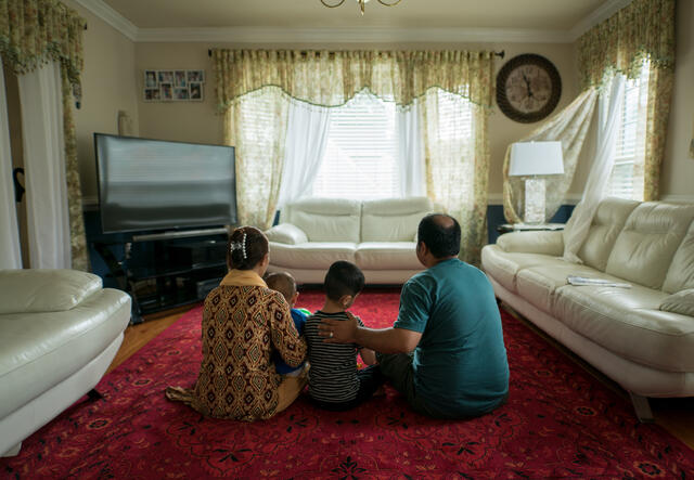 An Afghan family of three, including a woman, a man, and a young boy, in Richmond, Virginia sitting in their living room on the floor.