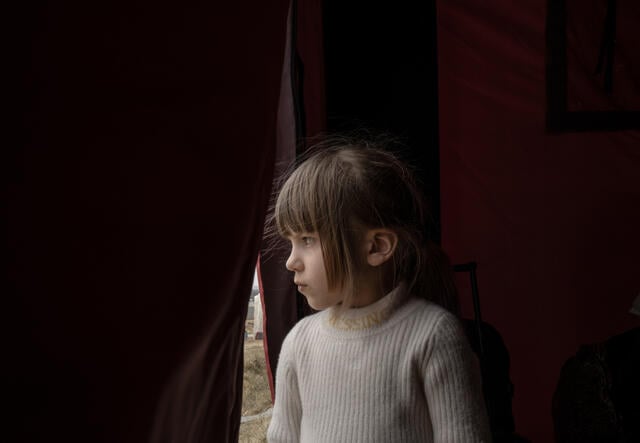 A young girl looks out the front entrance of a tent. 