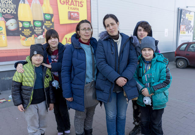 Two women and four children stand together in winter coats, facing the camera.