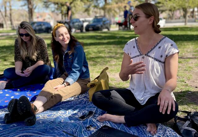 Group of women sitting on a tapestry outside talking about and discussing mental health.