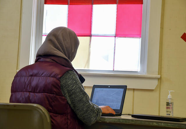 A woman looks at a laptop with her back turned to the camera 