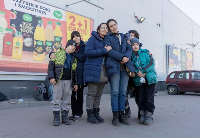 Two women surrounded by their children, all are wearing winter clothes and looking at the camera. 