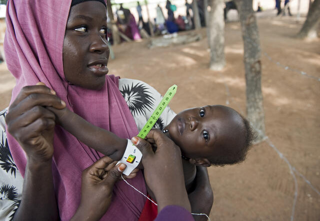 Mother holds child in displacement camp while undergoing medical tests