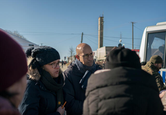 A man and woman stand amongst a crowd outside, wearing winter coats.